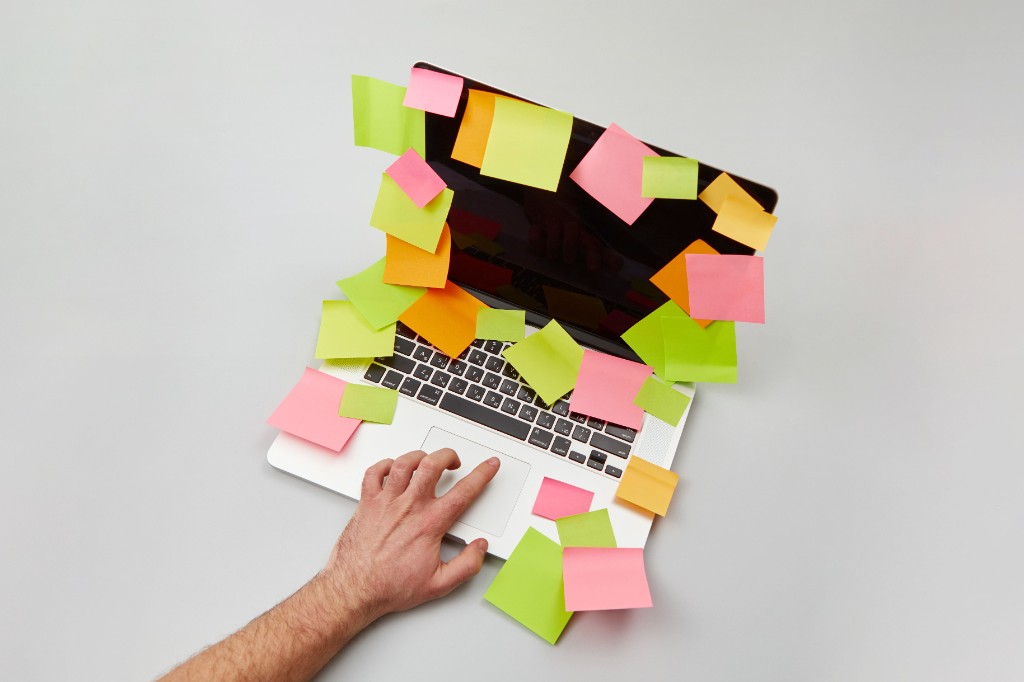Laptop covered in sticky notes, overwhelmed with tasks